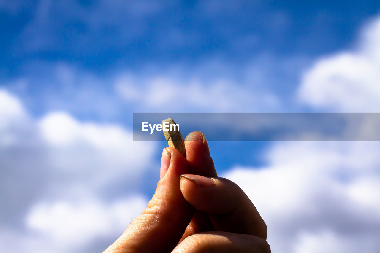 LOW ANGLE VIEW OF HUMAN HAND HOLDING SKY