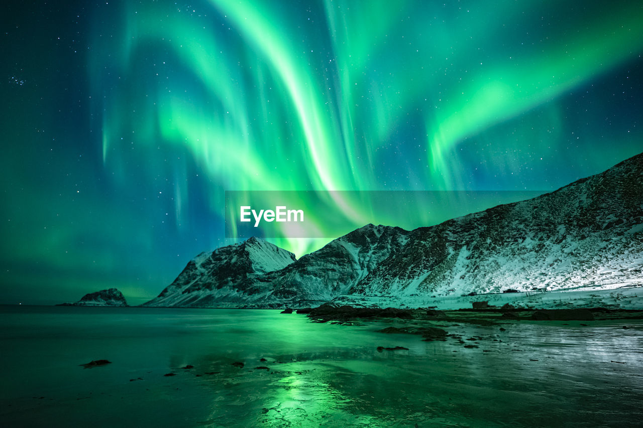 Aurora borealis over sea against sky at night