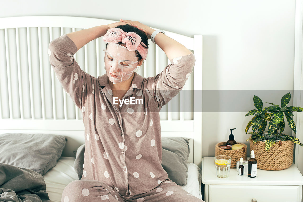 Woman with face mask while sitting on bed at home