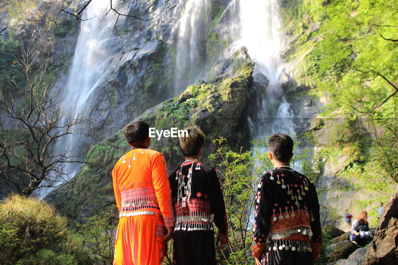 REAR VIEW OF MAN LOOKING AT WATERFALL IN FOREST