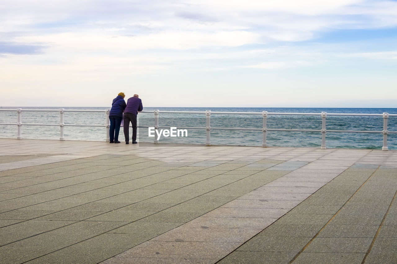 sea, sky, walkway, water, boardwalk, horizon over water, horizon, pier, two people, ocean, adult, men, shore, rear view, nature, coast, women, full length, vacation, railing, togetherness, beauty in nature, blue, scenics - nature, day, beach, cloud, lifestyles, leisure activity, tranquility, standing, love, tranquil scene, outdoors, land, holiday, bonding, sand, positive emotion, wood, trip, walking, female, emotion, footpath, architecture