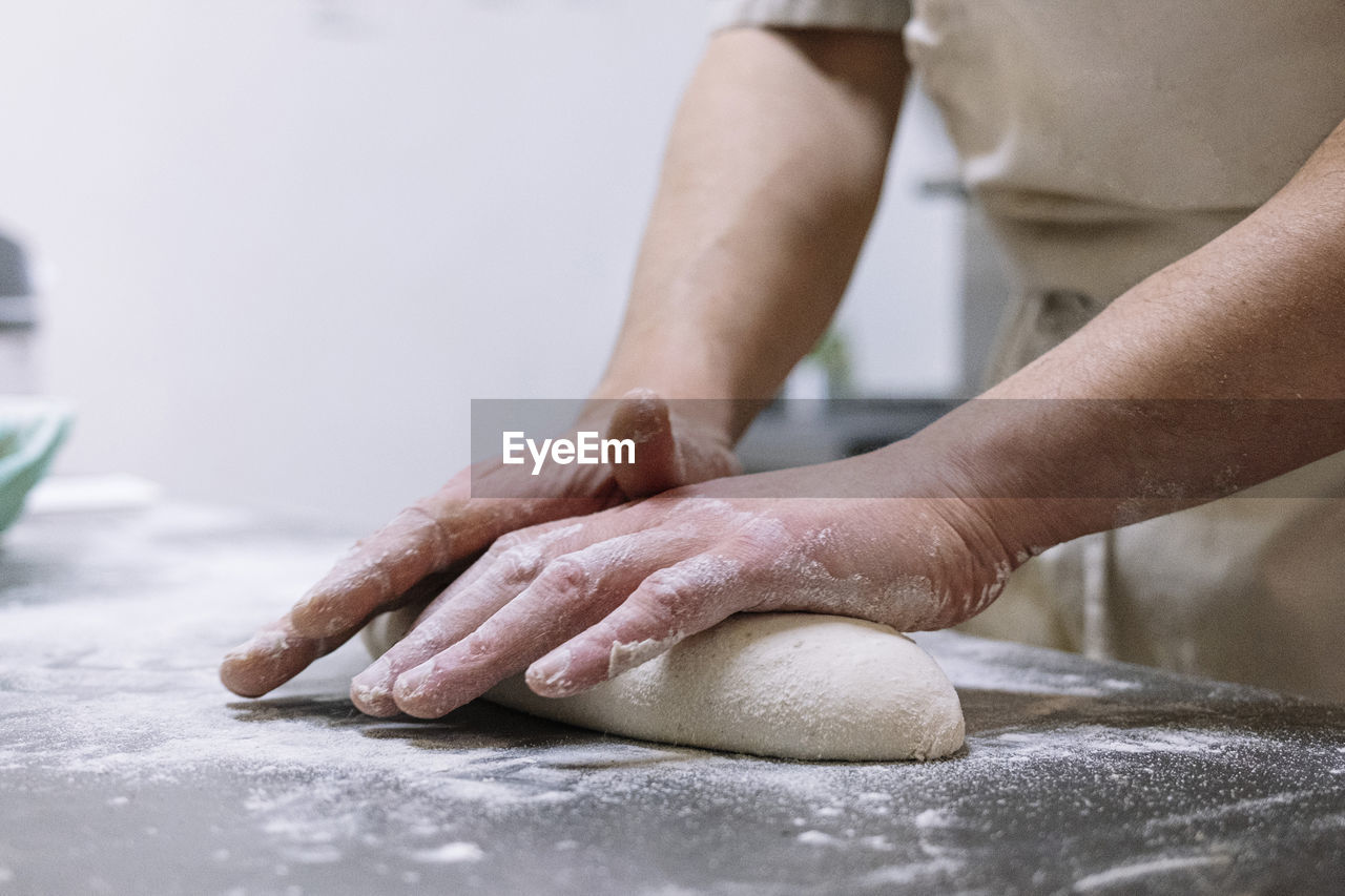 Male chef kneading flour dough on kitchen counter in bakery