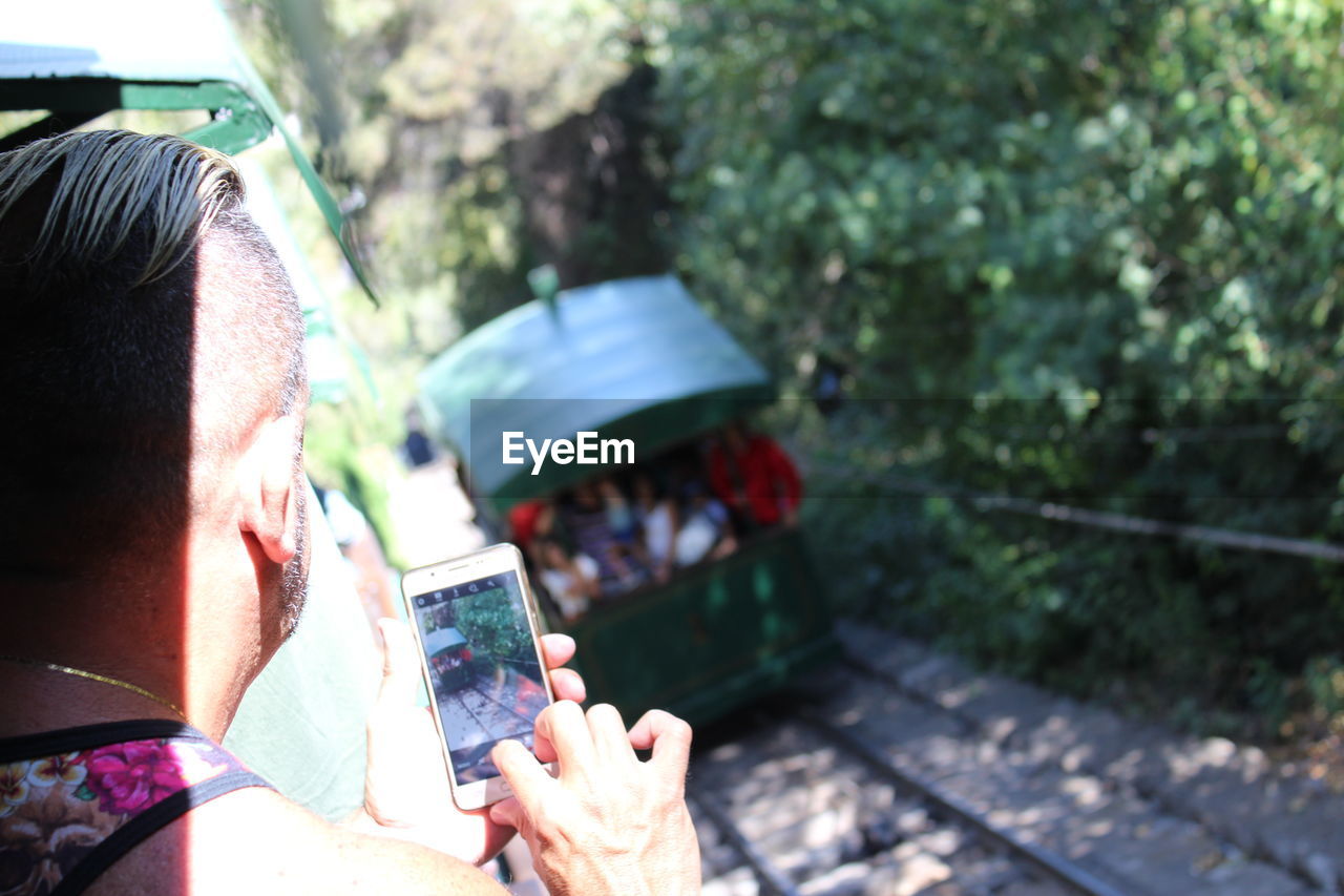 Rear view of man on passenger train photographing using mobile phone