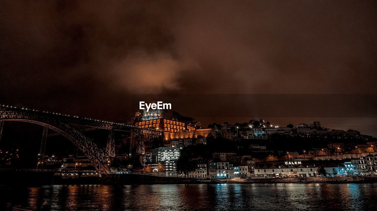 Illuminated buildings by river against sky at night