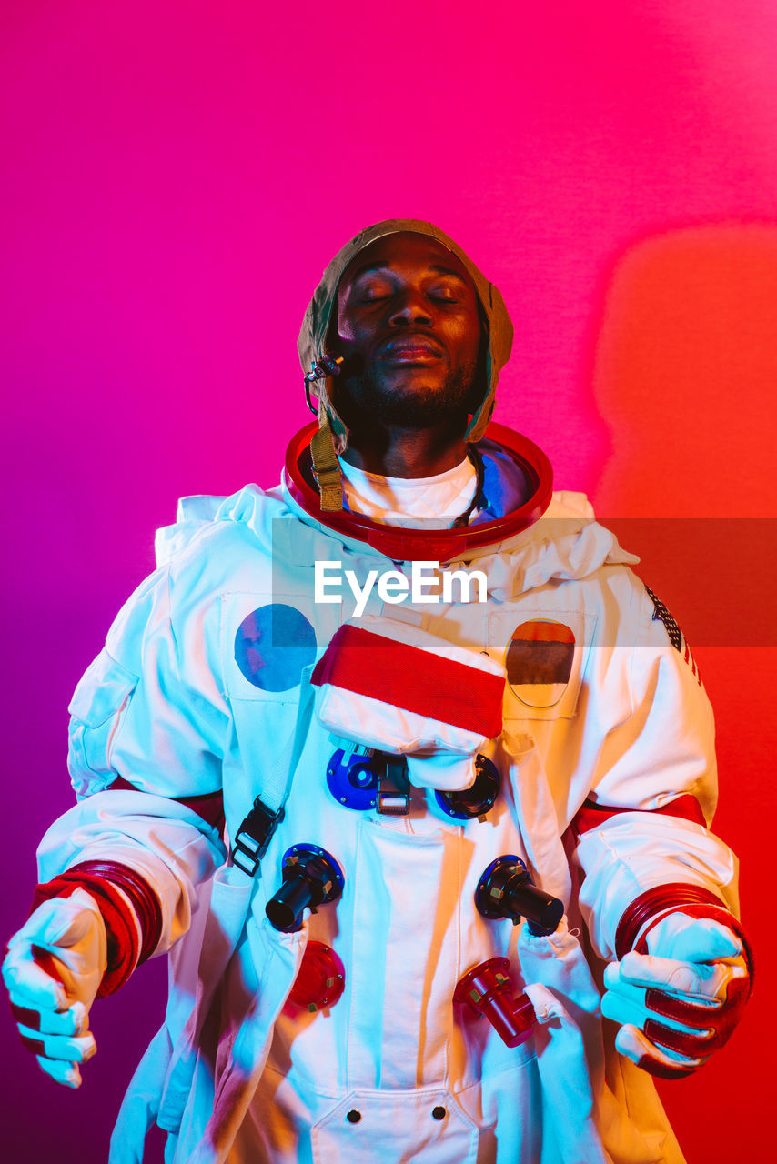 Smiling man wearing space suit standing against colored background