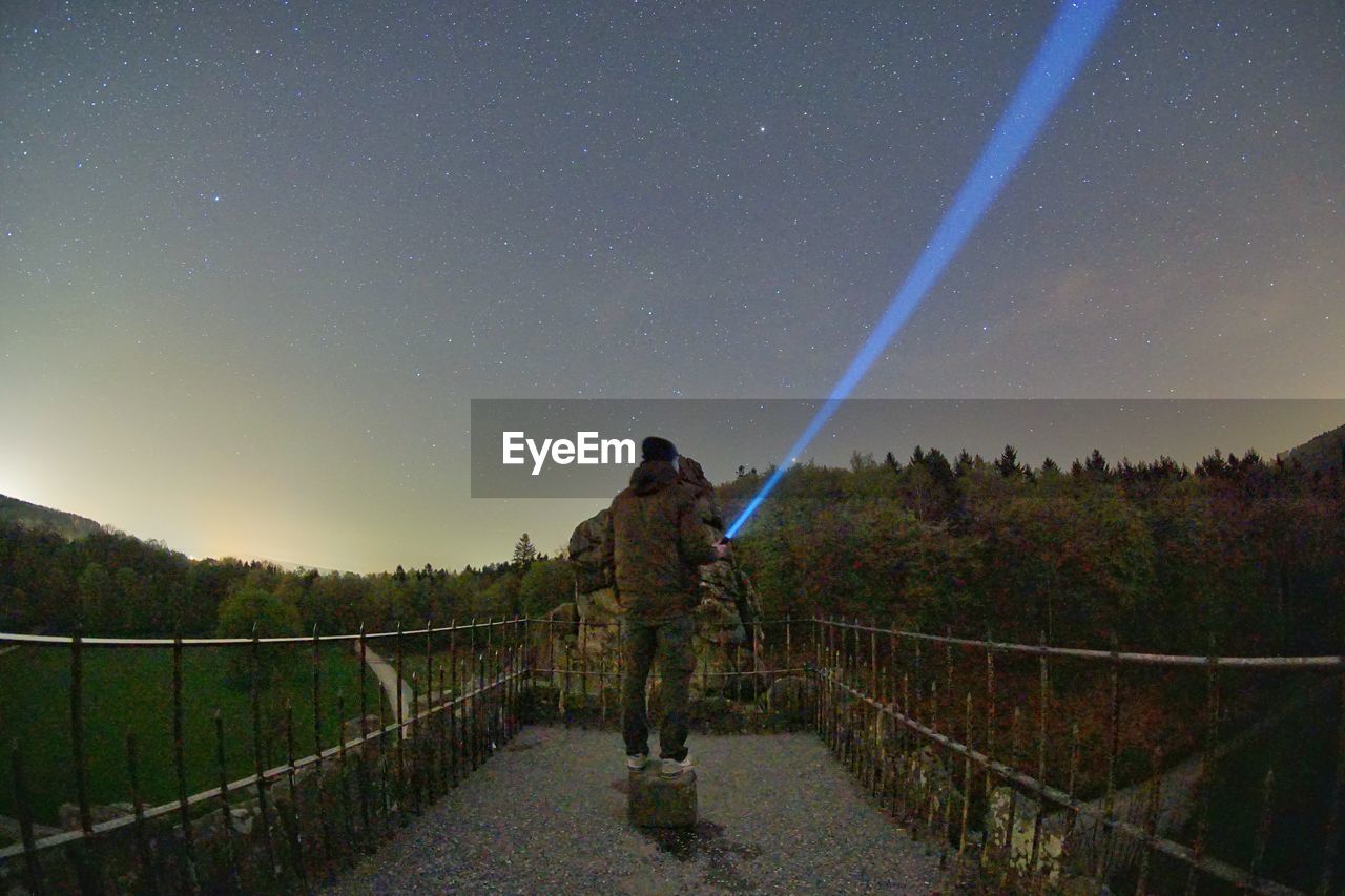 Man with flashlight standing on footbridge in city