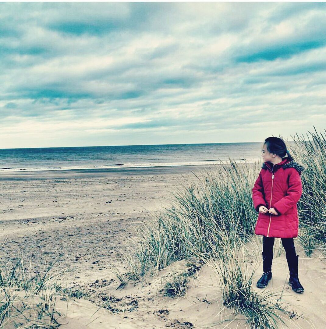 WOMAN STANDING ON BEACH AGAINST CLOUDY SKY