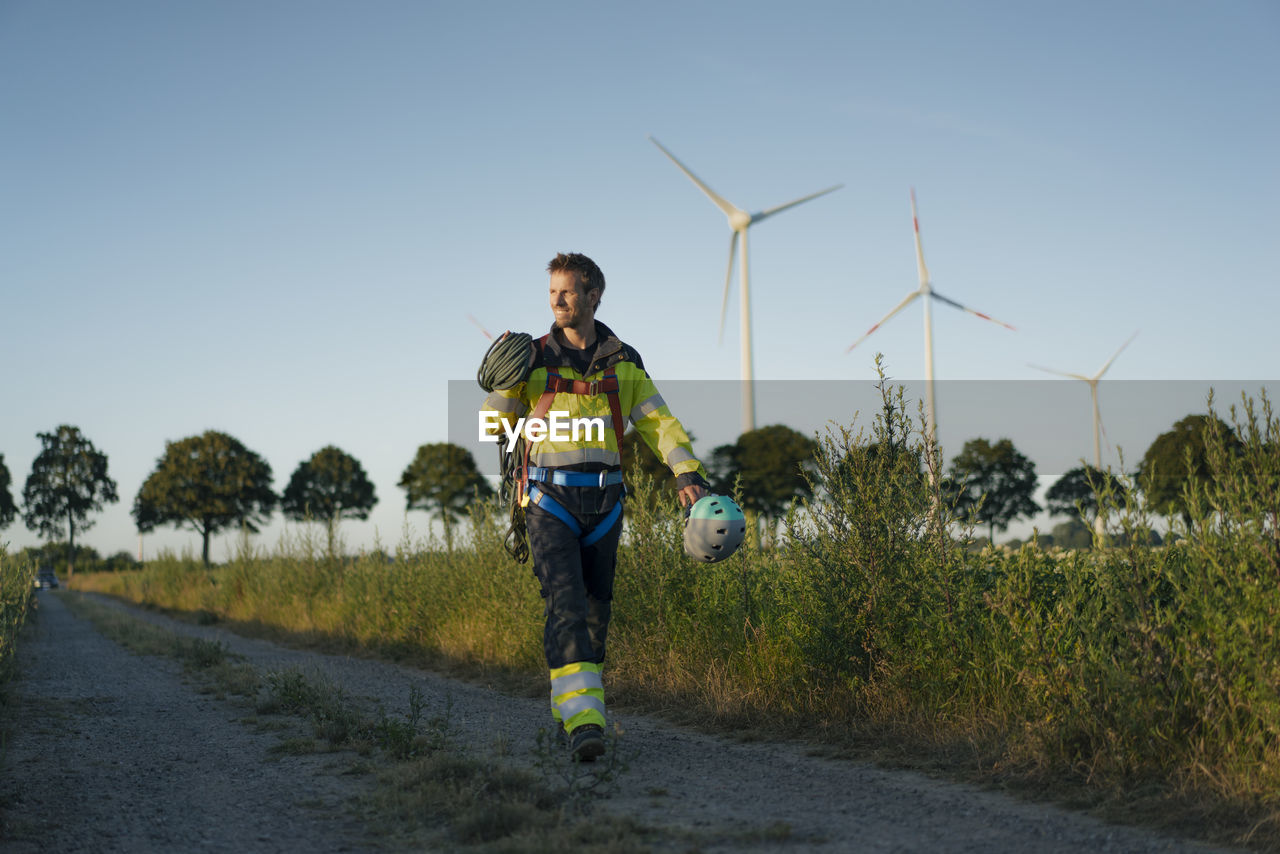 Technician walking on field path at a wind farm with climbing equipment