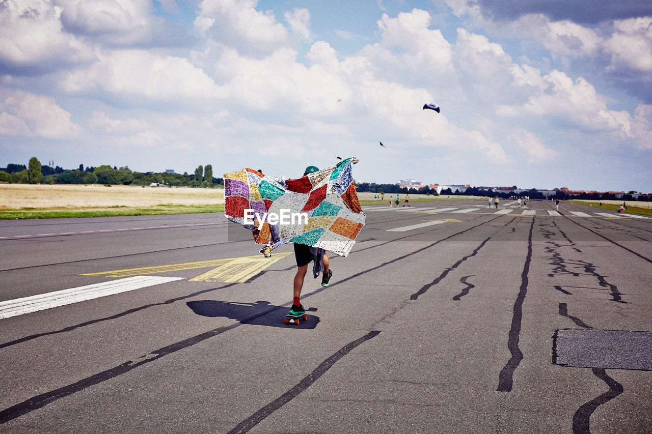 Rear view of person holding colorful shawl while skating on airport runway