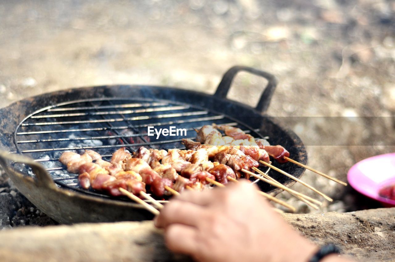 Cropped hand of person cooking meat on barbecue grill