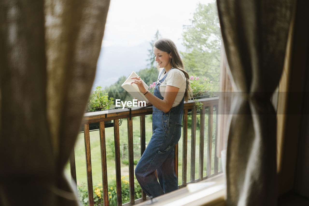 Happy woman reading book standing on balcony