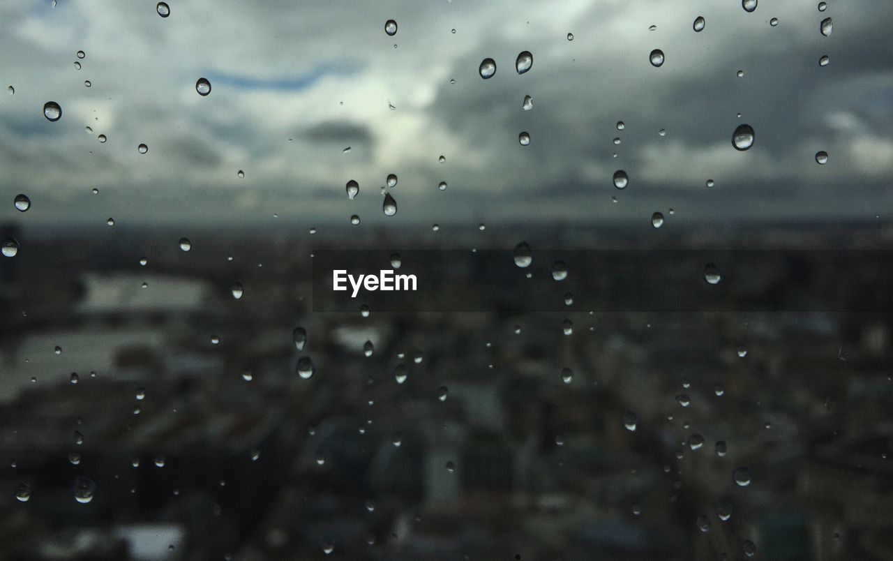 FULL FRAME SHOT OF WET GLASS WINDOW AGAINST SKY