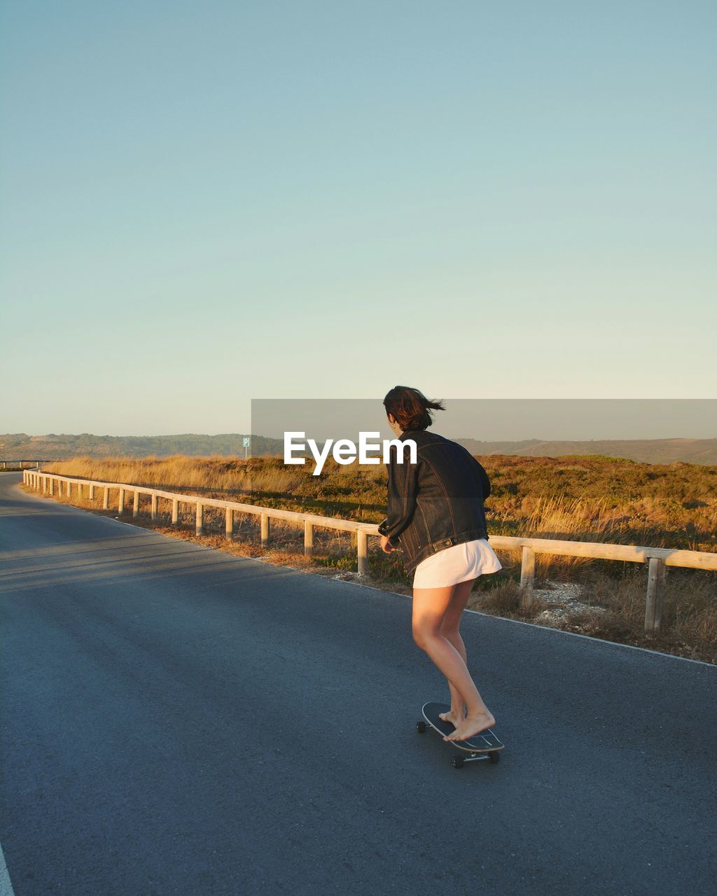 Woman skateboarding on road against blue sky