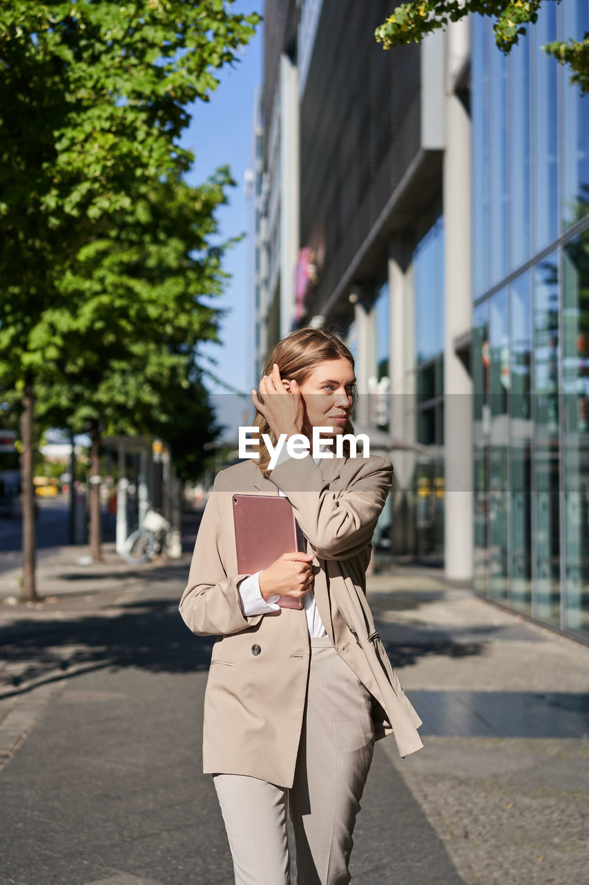 portrait of young woman standing against buildings in city