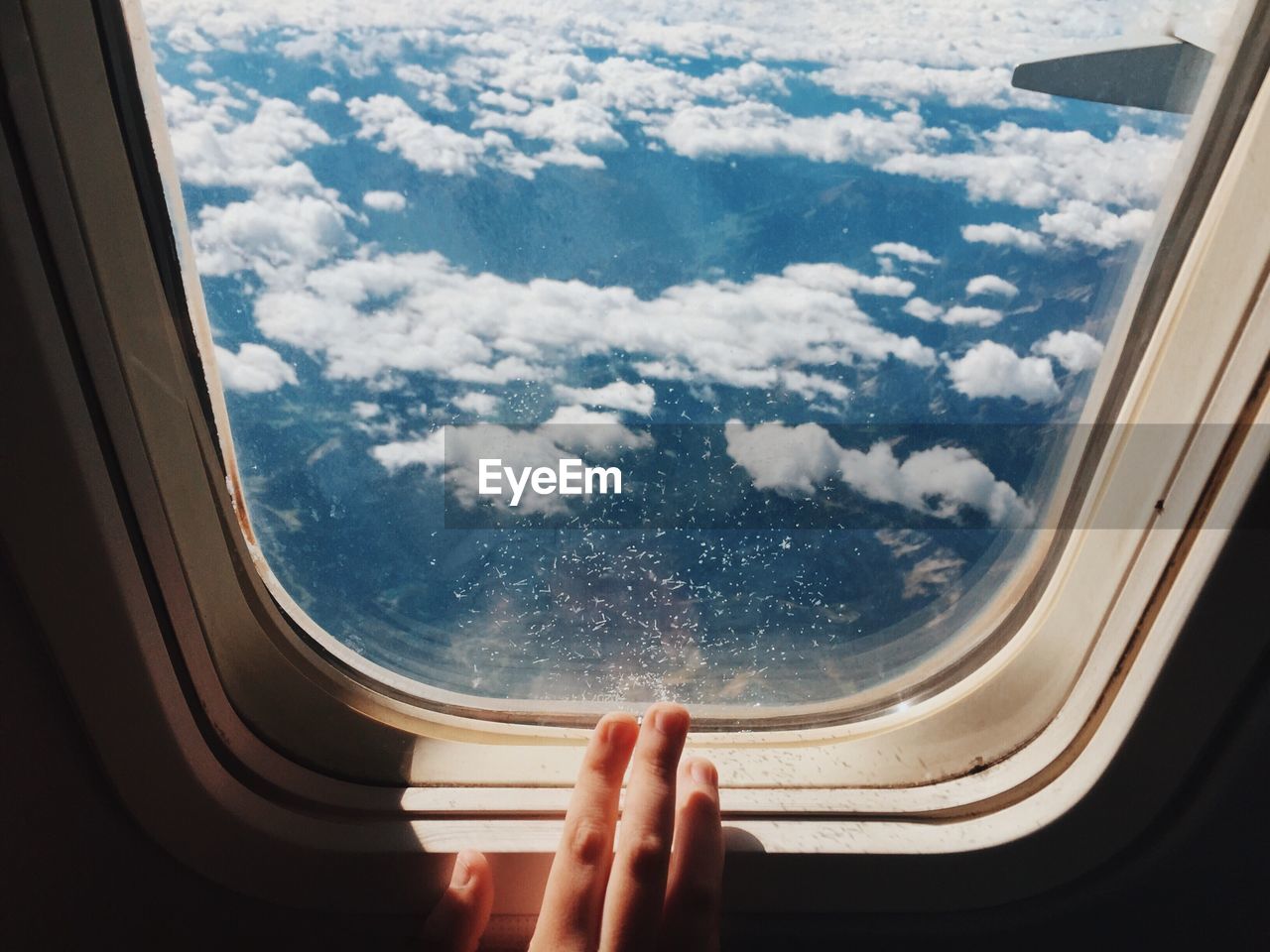 Cropped image of hand by airplane window against sky