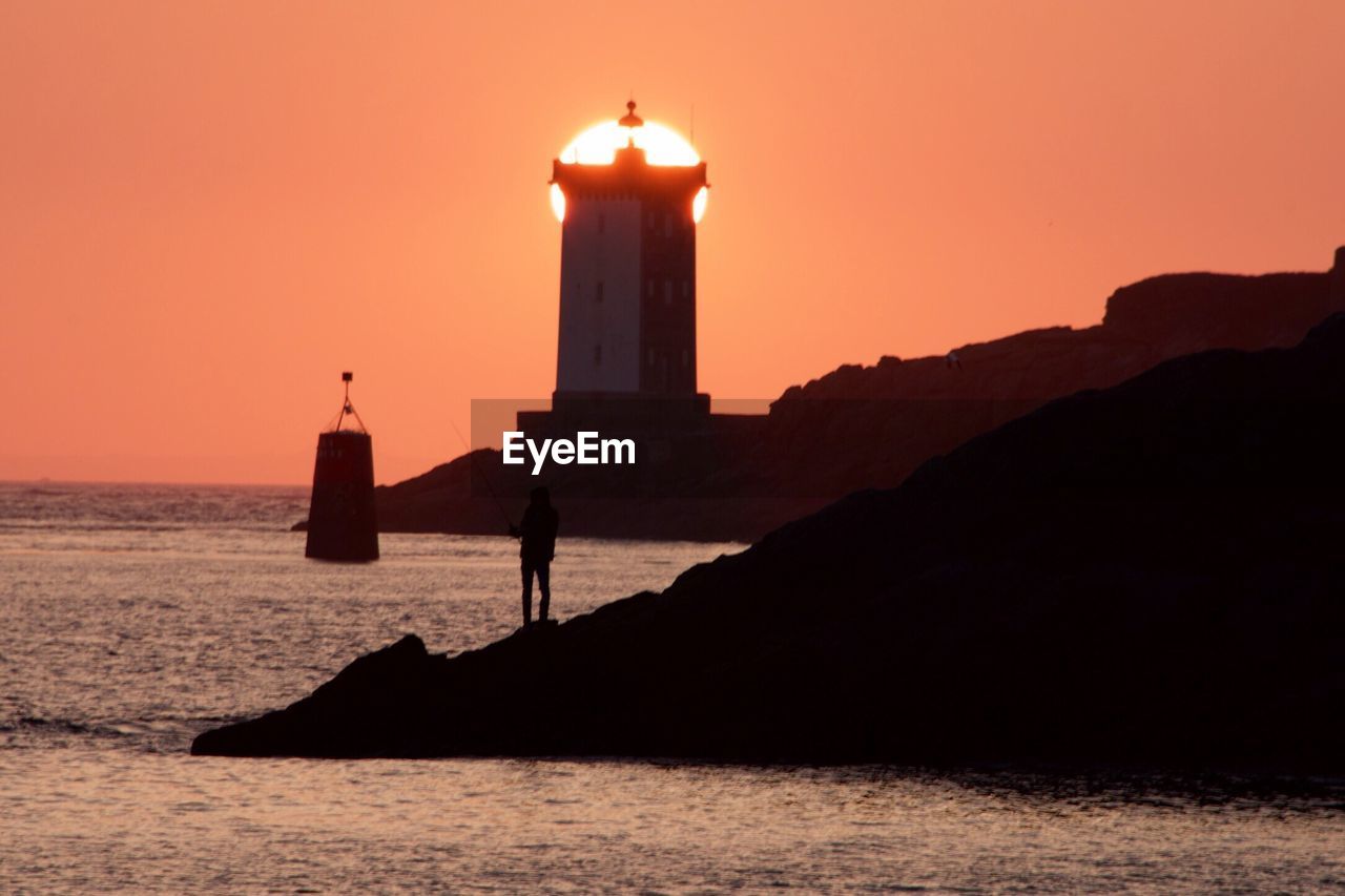 Silhouette lighthouse by sea against sky during sunset