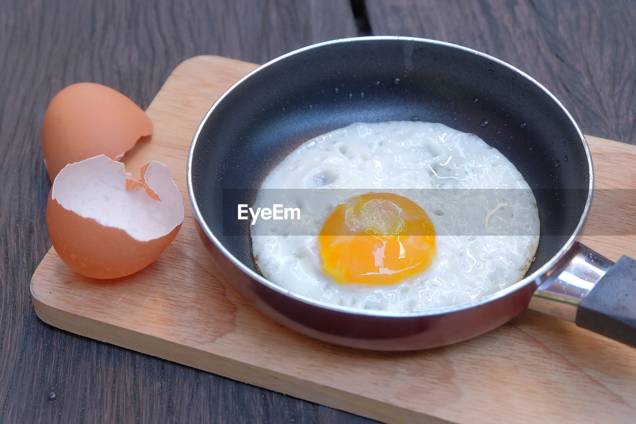 High angle view of egg in cooking pan on cutting board