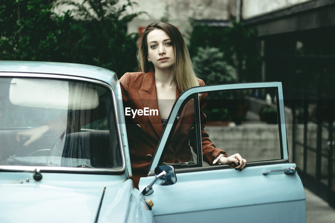 Portrait of woman standing with car on road