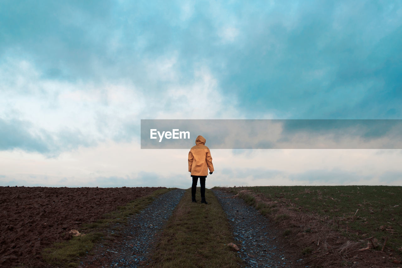 Man standing on road against cloudy sky