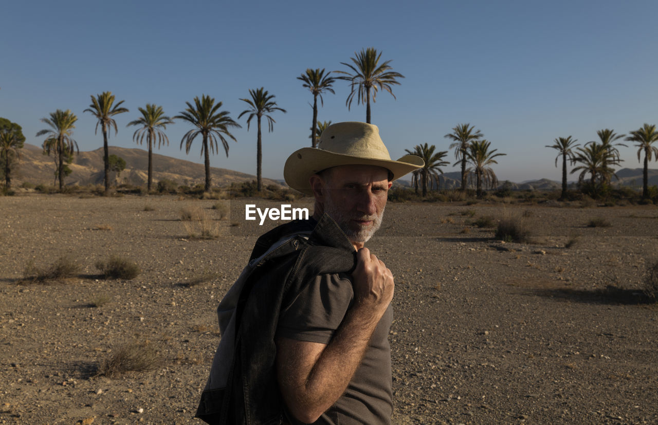 Adult man in cowboy hat on tabernas desert with palm trees against blue sky. almeria, spain