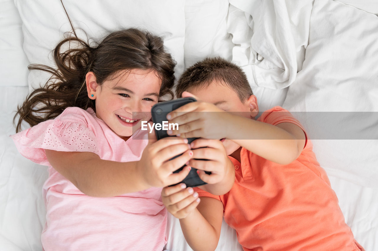 young woman using phone while lying on bed at home