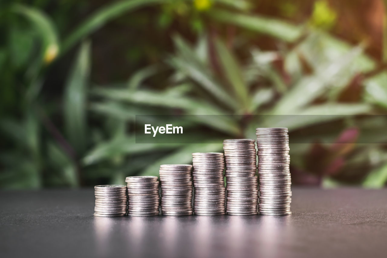 Close up of stacked rows of coins on a table with green leaves in the garden background