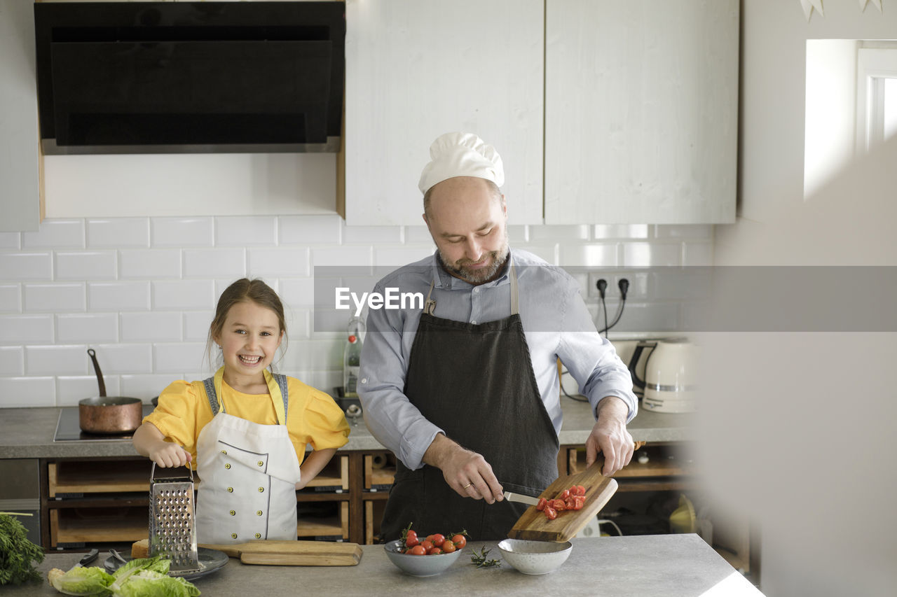 Smiling daughter standing by father preparing food in kitchen at home