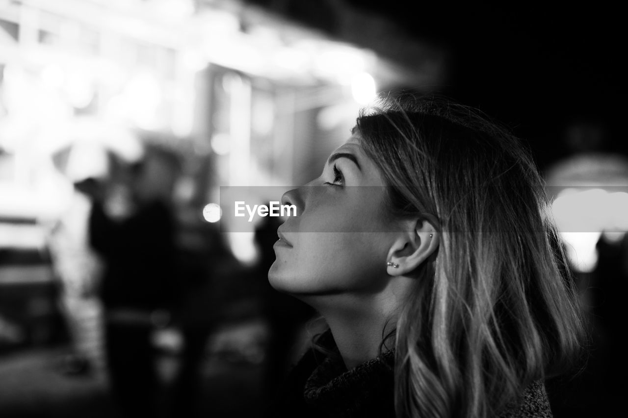 Close-up of thoughtful young woman looking up while standing on street at night