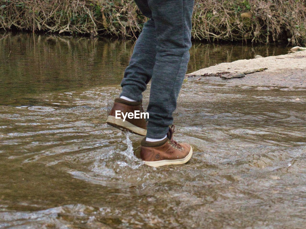 LOW SECTION OF PERSON STANDING ON ROCK AT RIVERBANK