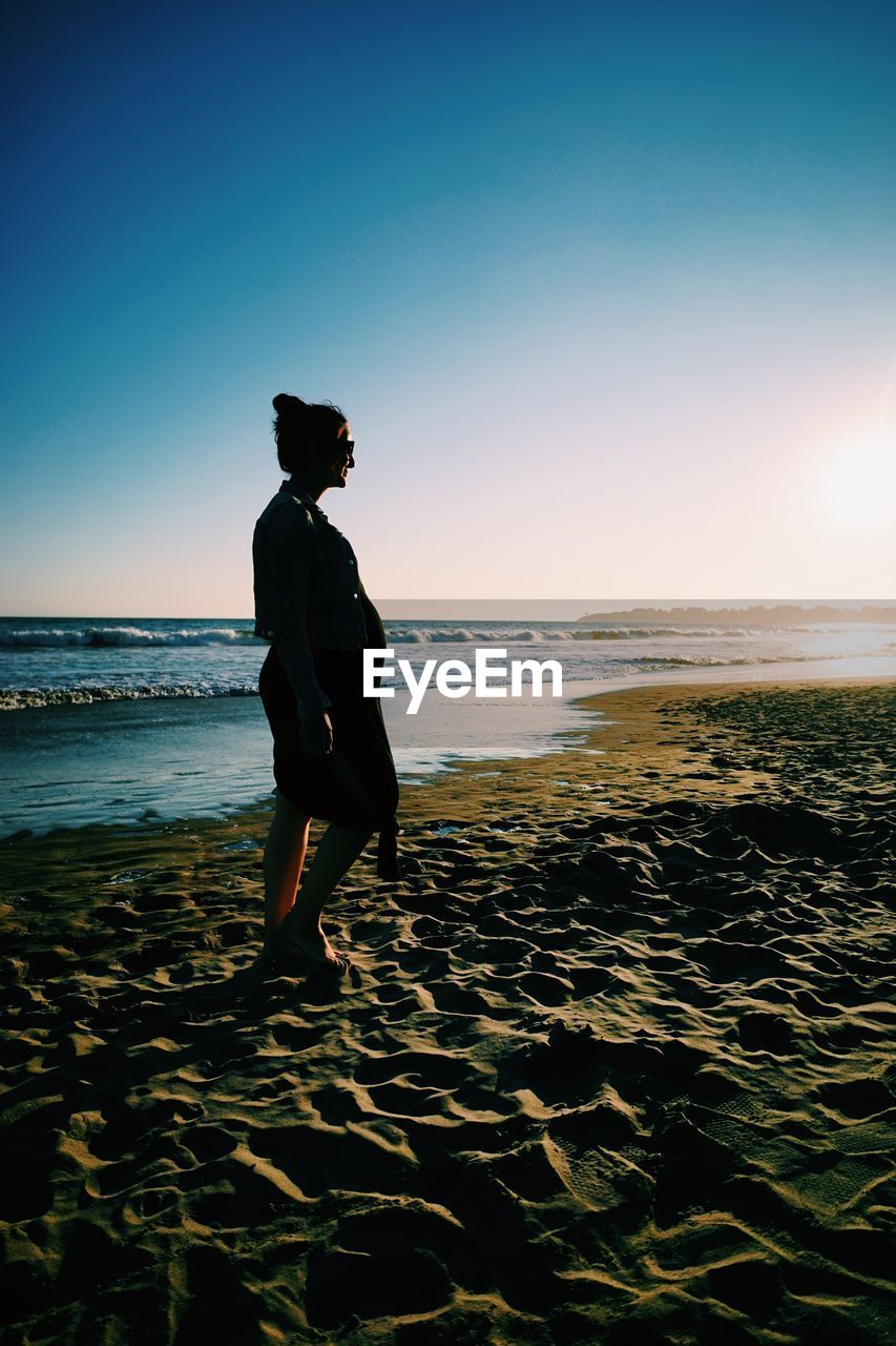 Full length of woman standing on beach against sky during sunset