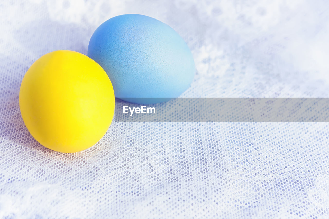 Two painted yellow and blue easter eggs close-up on a white vintage lace tablecloth. space for copy.