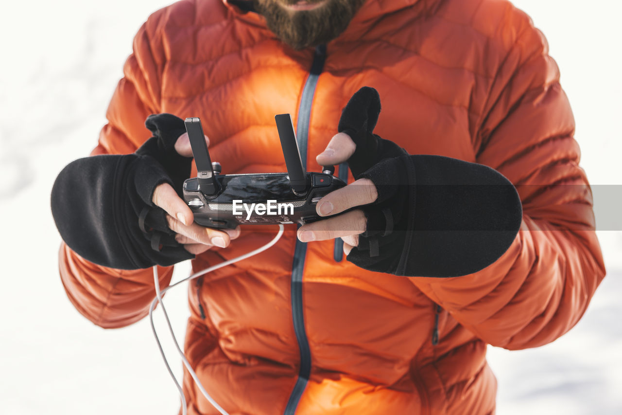 Man using remote control while standing on snow covered field