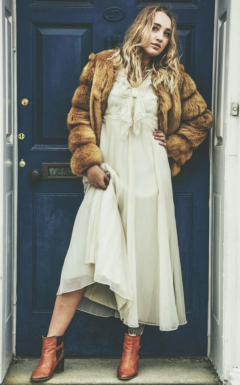 Full length portrait of fashionable young woman standing against closed door