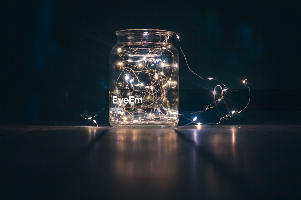 CLOSE-UP OF ILLUMINATED GLASS JAR ON TABLE