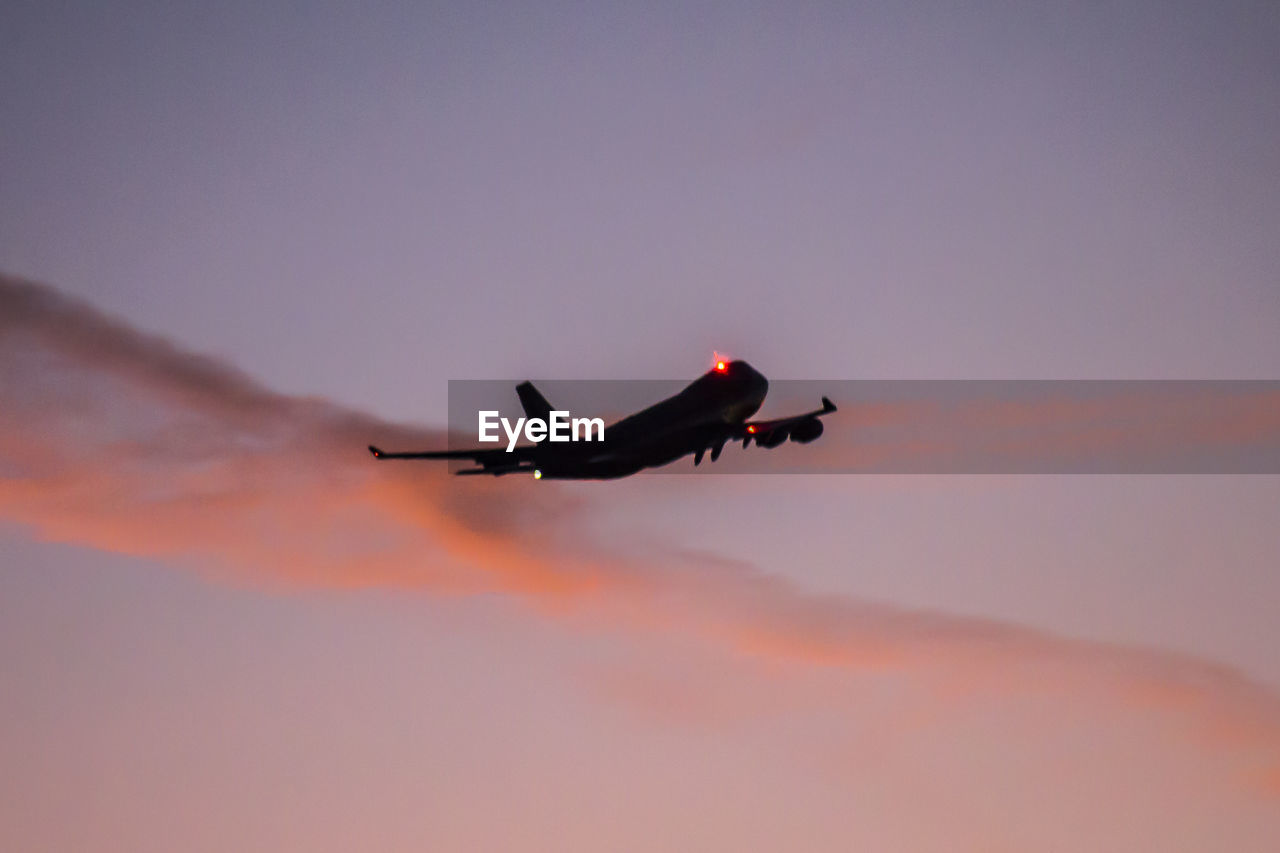 Low angle view of airplane flying against sky during sunset