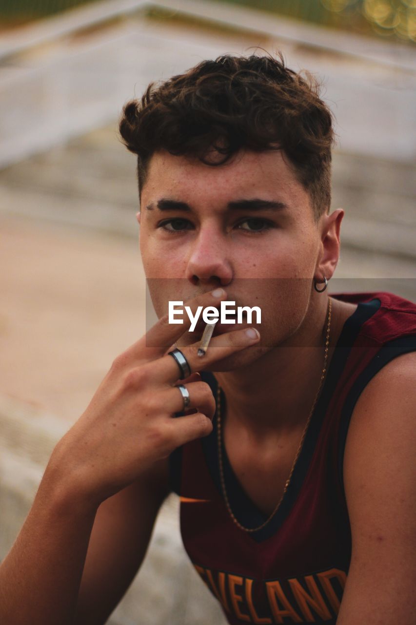 Portrait of young man smoking cigarette sitting outdoors