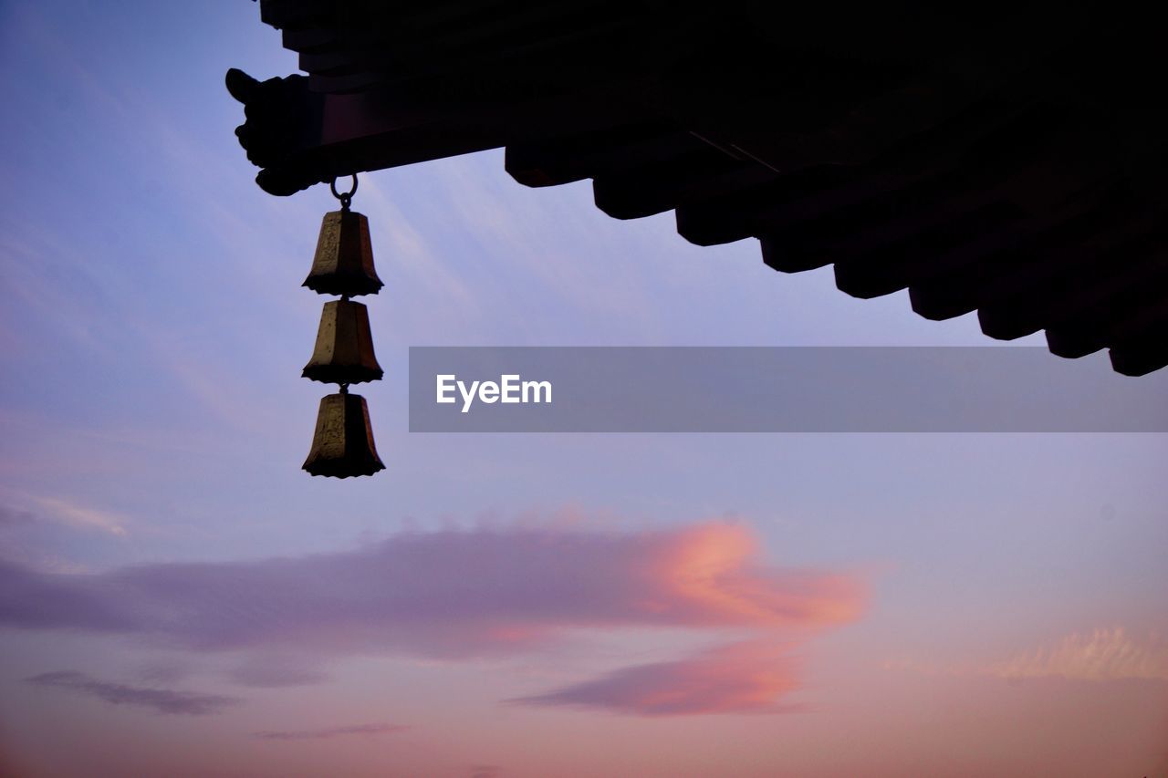 Low angle view of bells hanging from roof against sky during sunset