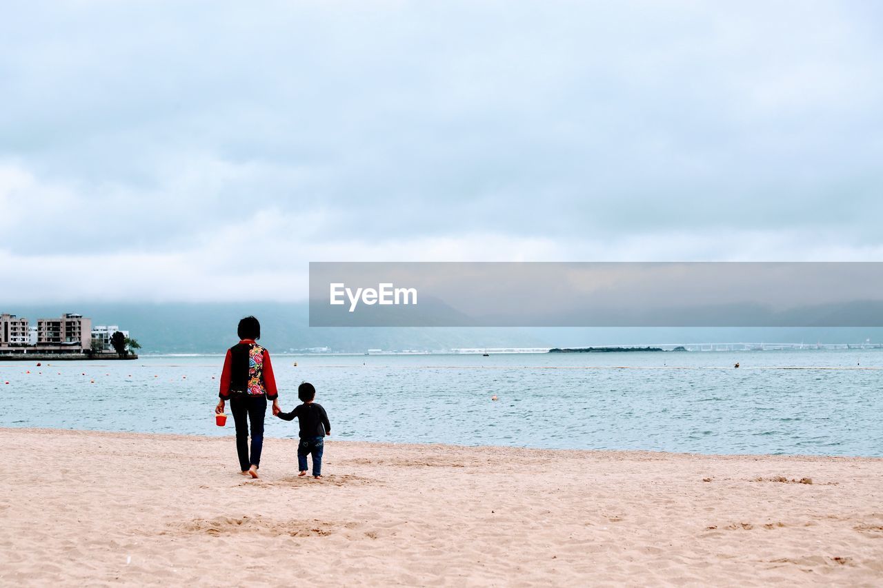 Rear view of people enjoying at beach against sky