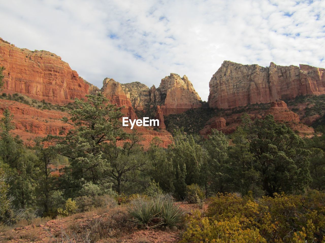 Red rock formations on landscape against cloudy sky