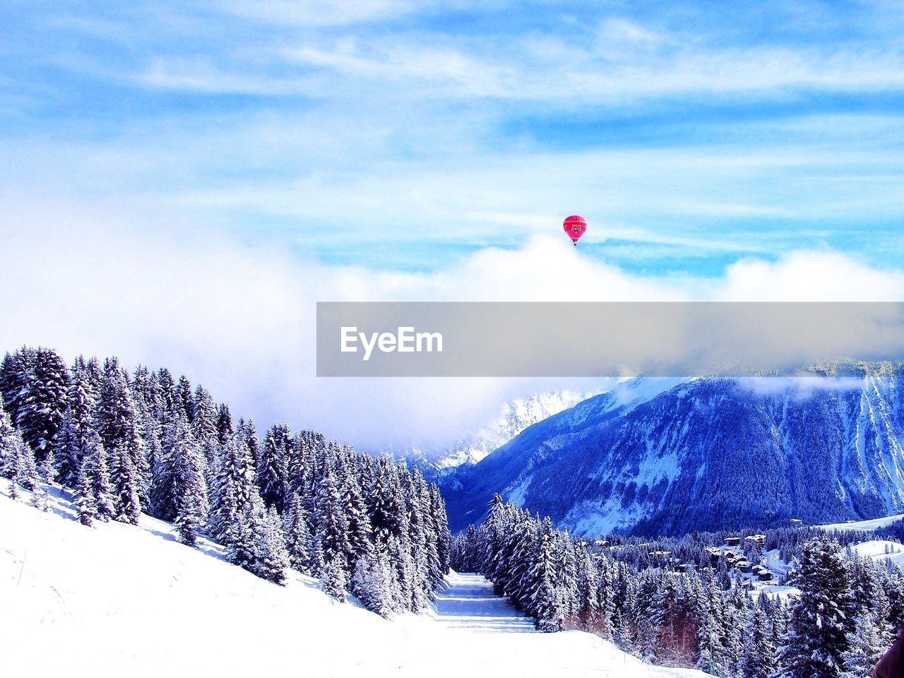 Red hot air balloon over snowcapped mountains against cloudy sky