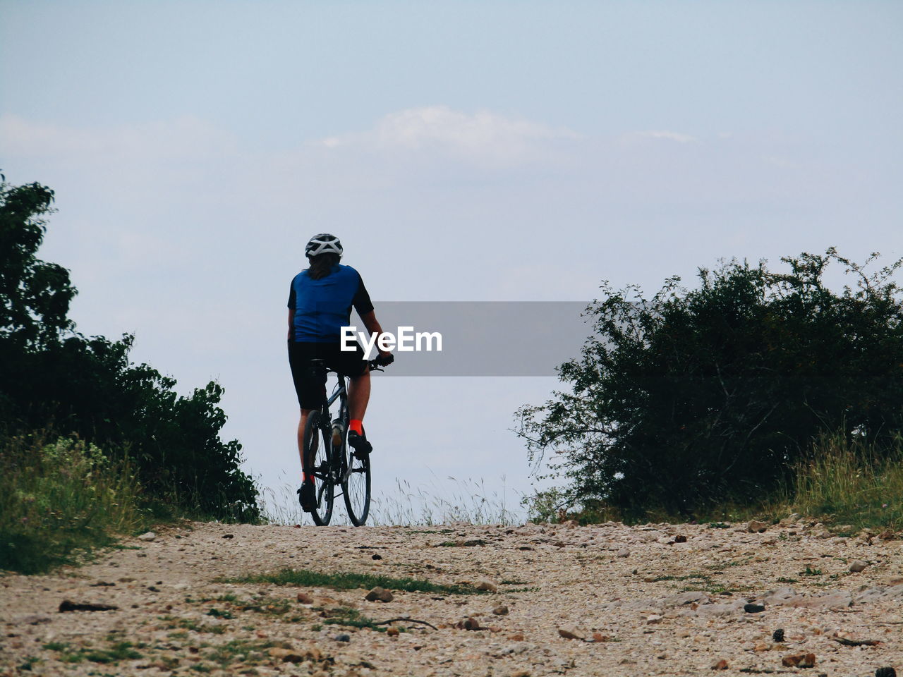 REAR VIEW OF MAN RIDING BICYCLE AGAINST SKY