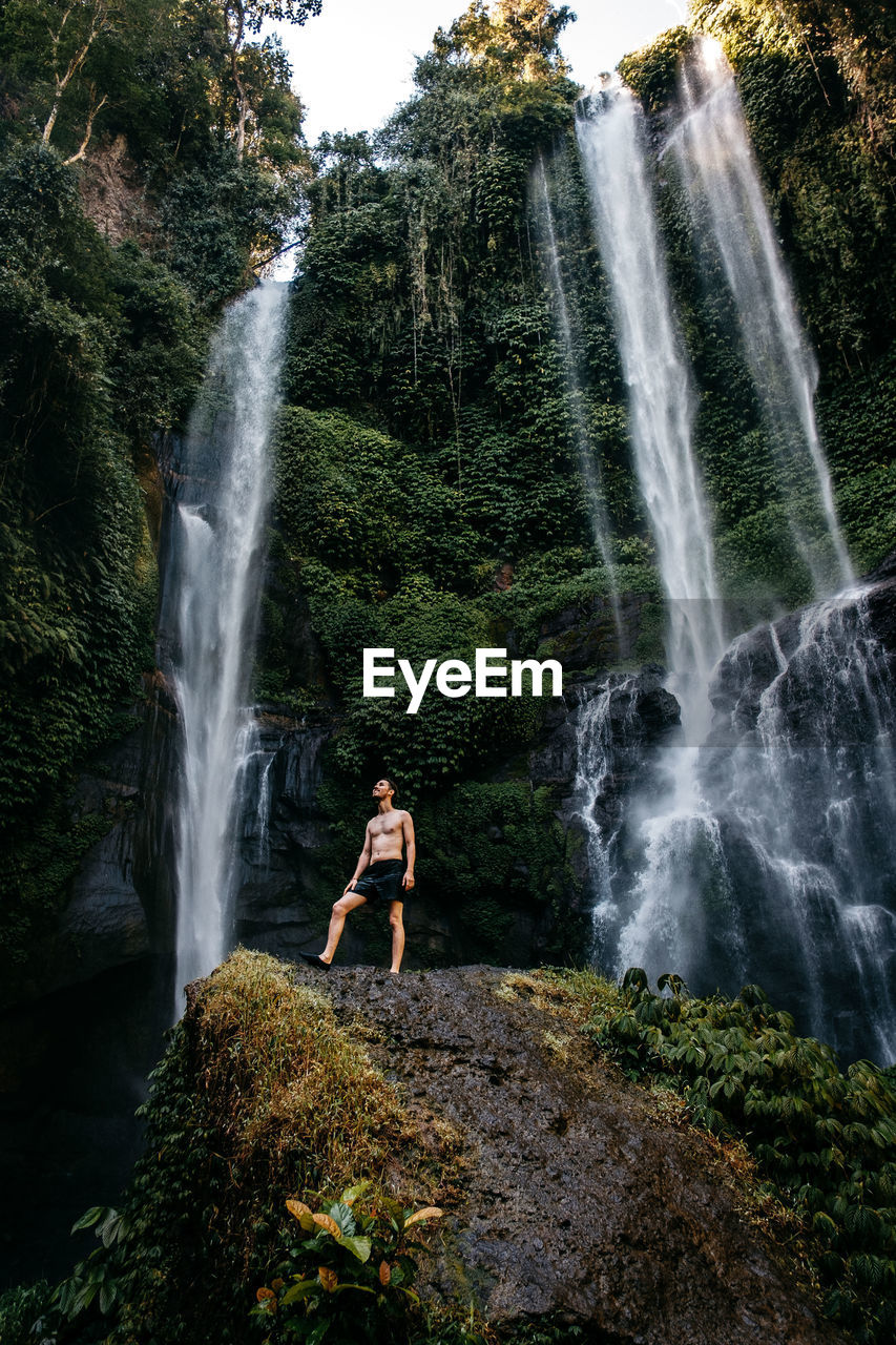 Man standing on rock against waterfall in forest