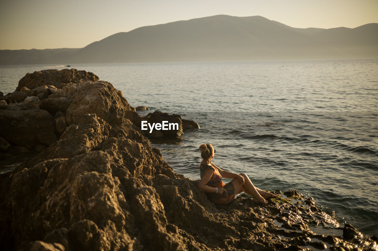 rear view of man sitting on rock at beach