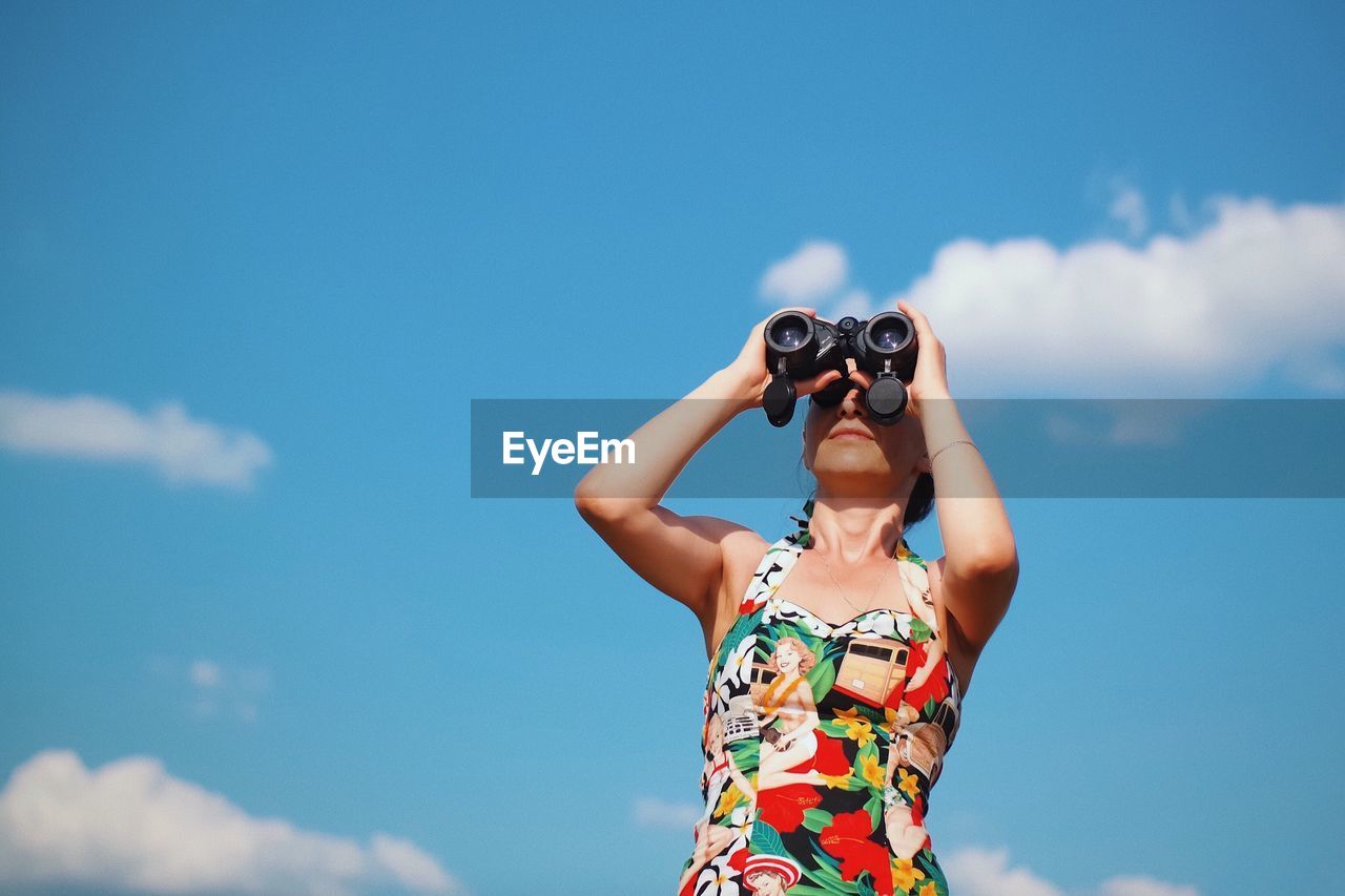 Low angle view of woman looking through binoculars against blue sky