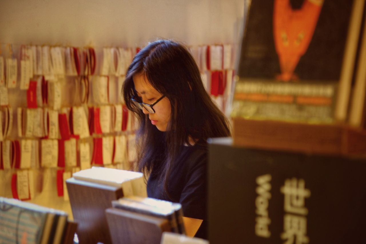 YOUNG WOMAN LOOKING AWAY WHILE BOOK ON SHELF