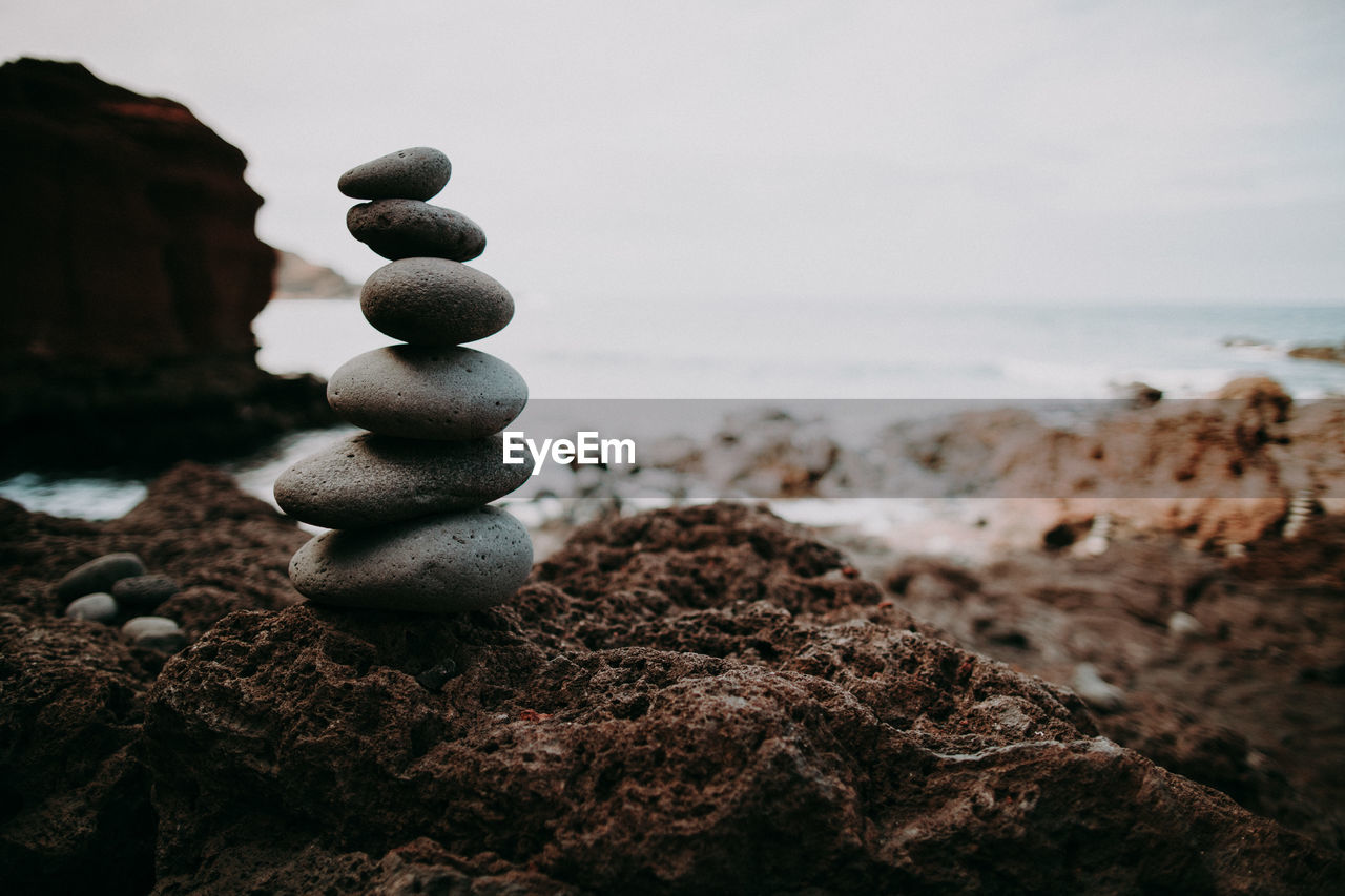 Stack of stones on rock at beach against sky