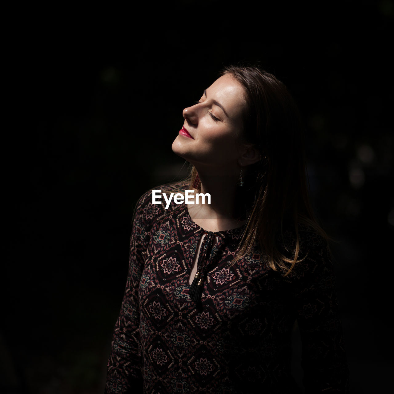 Woman with eyes closed standing against black background