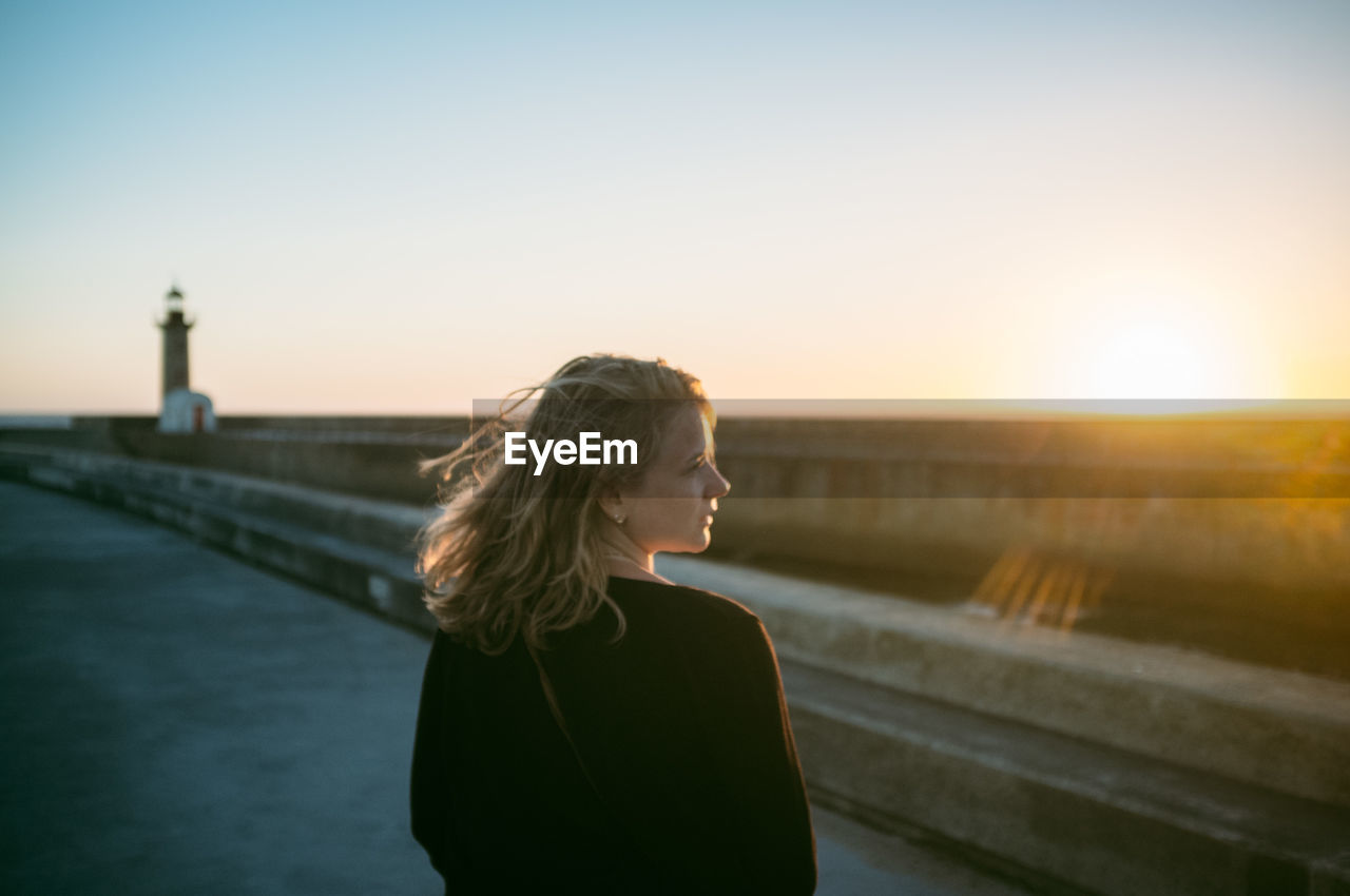 Woman looking away at promenade against clear sky during sunset