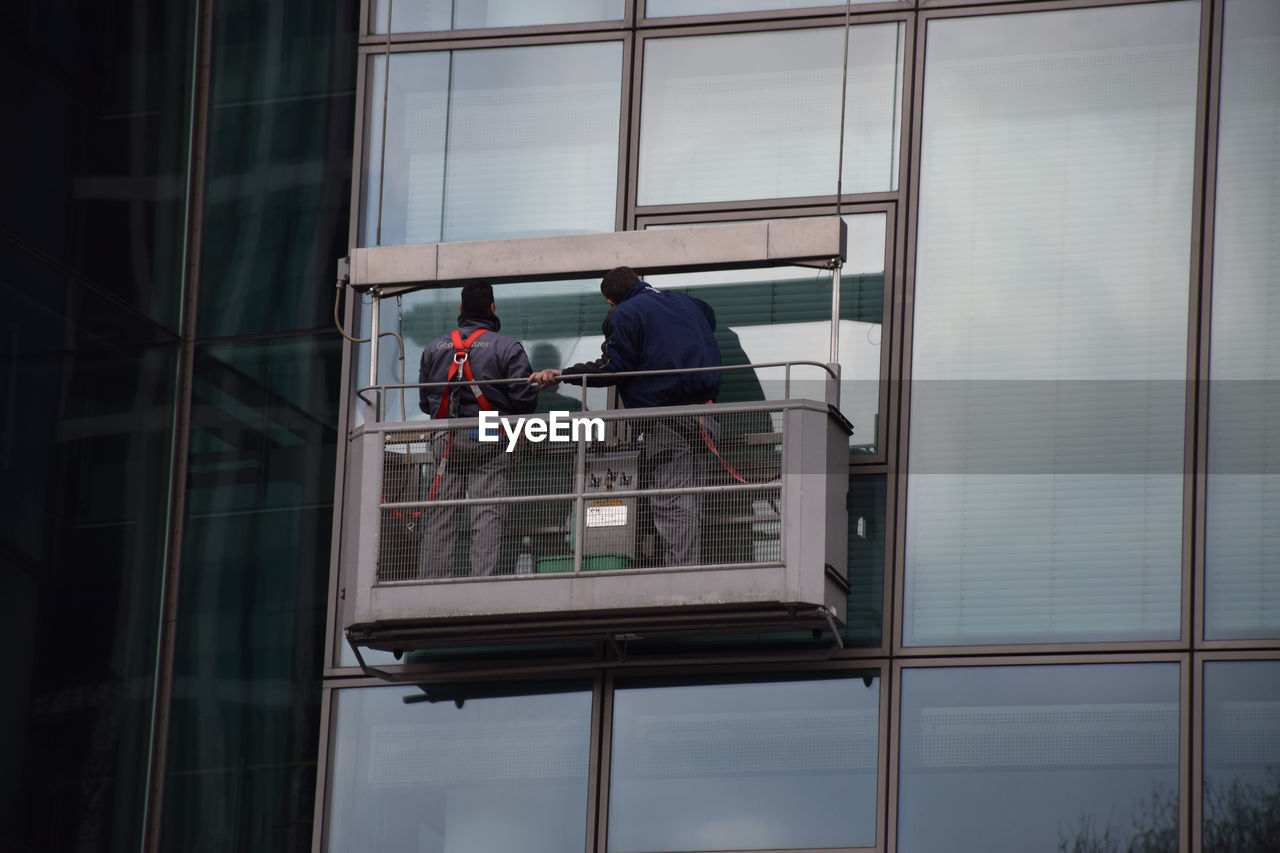 Low angle view of window washers cleaning glass building