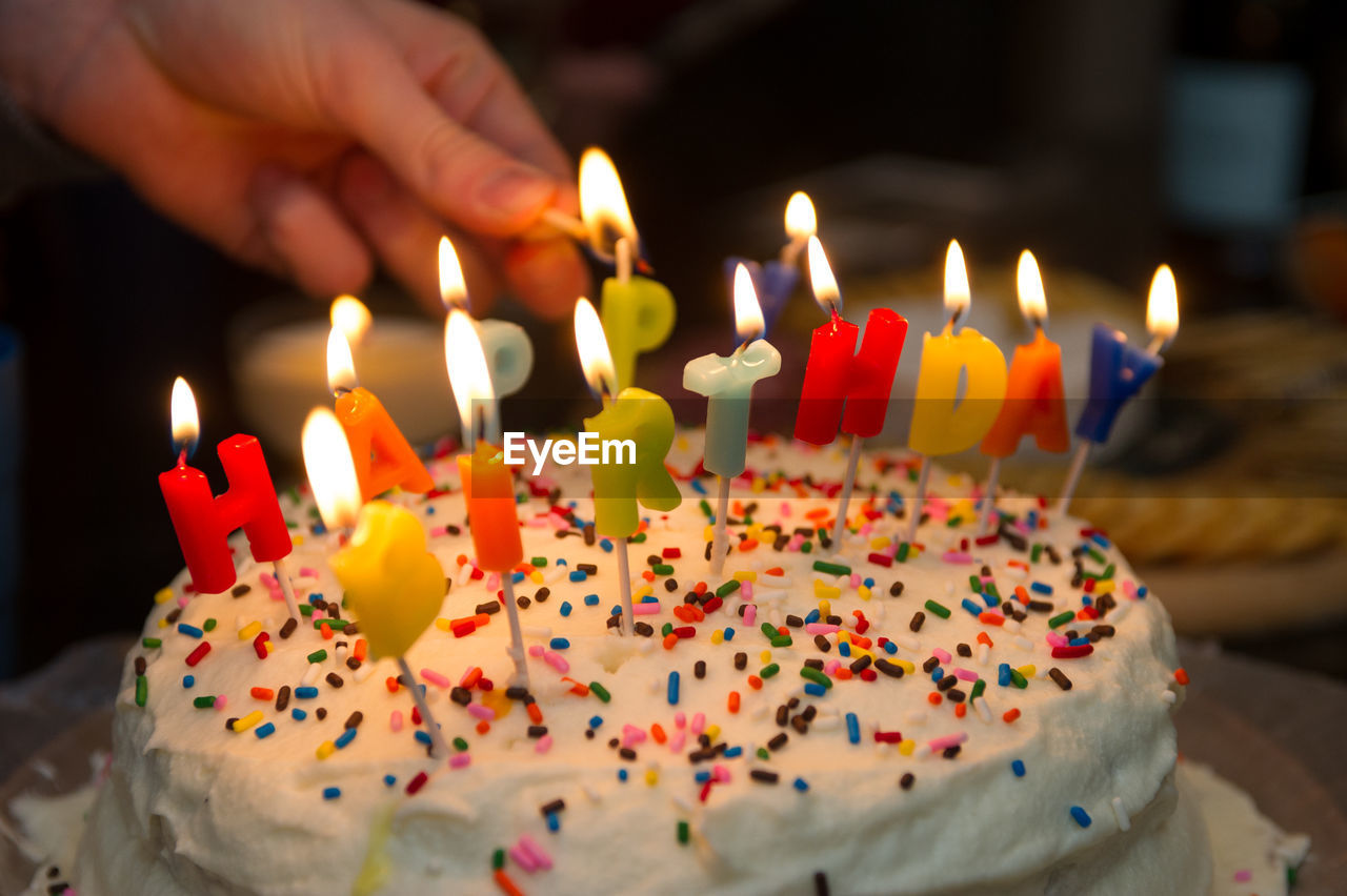 Cropped hand of person burning candle on birthday cake